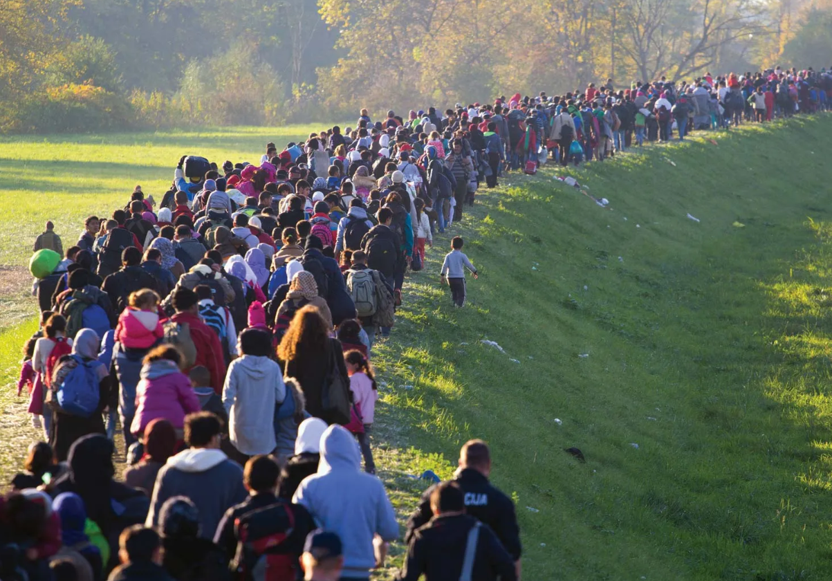 A large group of people walking together along a grassy path