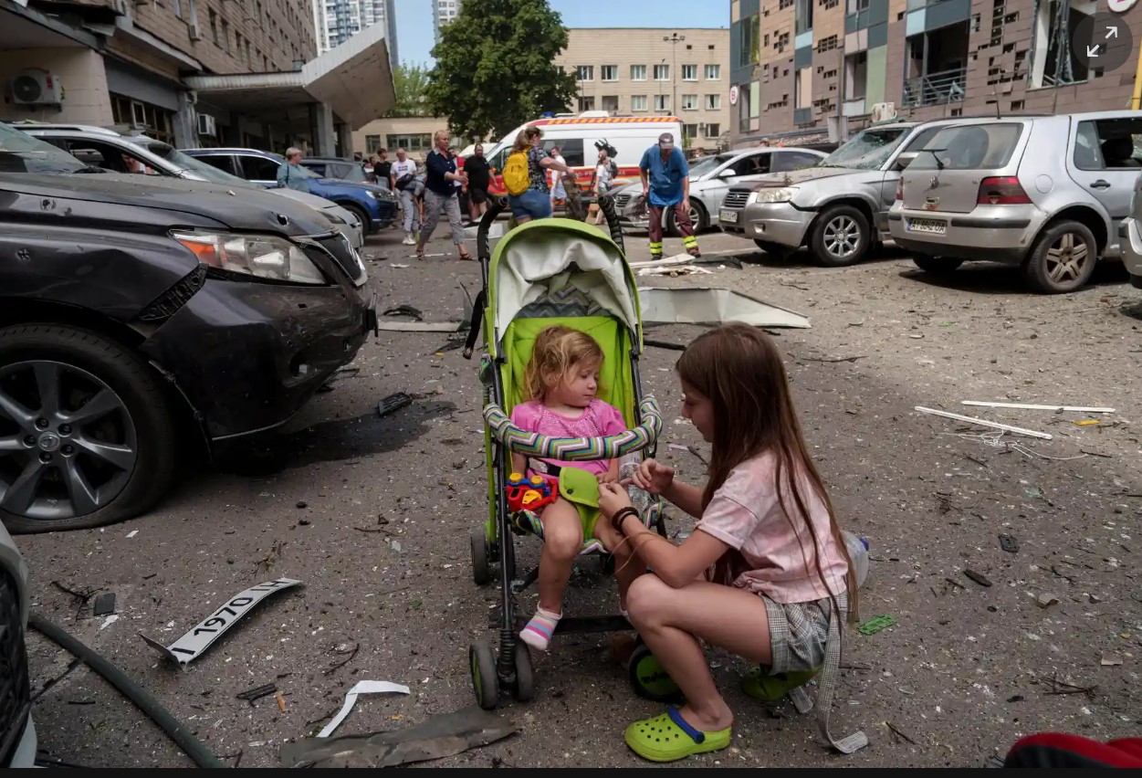 Two children and their caregiver outside a damaged hospital building in Kyiv after an attack.