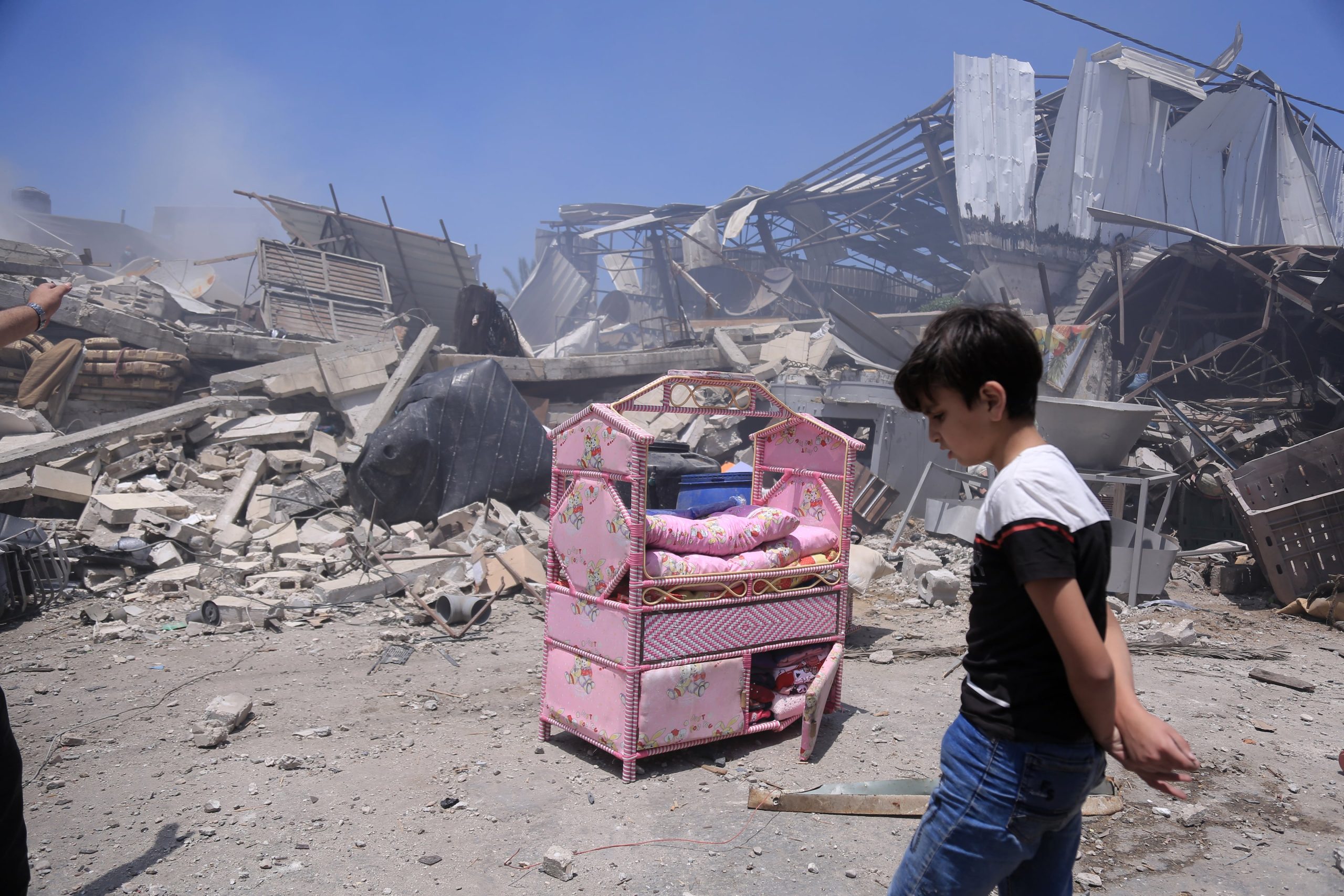 A Palestinian boy beside a pink cot and belongings near the ruins of a home in Gaza City