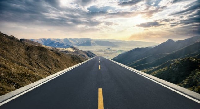 Mountain road leading toward sunlight on the horizon
